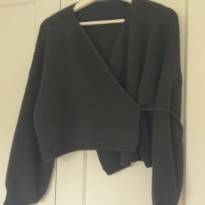 Svart omlott kofta med knytband - Svart stickad omlott kofta med knytband i midjan och långa ärmar. Bara använd en gång ❤️den är onesize men passar nån bra som har S.