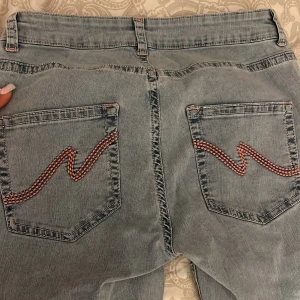 Ljusblå bootcut jeans från Nelly - Ljusblå jeans från Nelly med bootcut passform och slitna hål på knäna. Snygga röda broderade detaljer på bakfickorna och klassisk femficksdesign. Jeansen har hög midja och är tillverkade i jeansmaterial med en relaxed vibe.