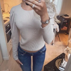 Beige ribbad långärmad tröja - Säljer en beige ribbad tröja med puffiga axlar och lång ärm. Tröjan har en rund halsringning och är figurnära i modellen, perfekt för dig som gillar en stilren och trendig look. Strl xs/s