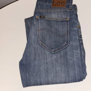 Blå jeans från Lee med raka ben W31 L32 - Säljer ett par klassiska blå jeans från Lee med raka ben och femficksdesign. Jeansen har en snygg tvättad look med diskreta slitningar och Lee-logga på bakfickan. Tillverkade i slitstarkt denimtyg som ger en tidlös vibe. W31 L32