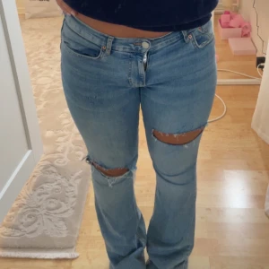 Ljusblå bootcut jeans med slitningar pris diskuteras  - Säljer ett par ljusblå jeans med bootcut-modell och snygga slitningar över knäna. Jeansen har klassisk femficksdesign, normal midja och är tillverkade i jeansmaterial. Perfekta för en avslappnad och trendig look.