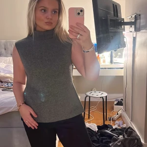 Grå stickad polotopp med slits - Säljer en grå stickad polotopp utan ärmar. Toppen har en hög polokrage och en snygg slits i sidan. Mjuk och skön känsla. Säljs då den inte kommer till användning🩷