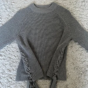 Grå stickad tröja med snörning - Säljer en grå stickad tröja med snygg snörningsdetalj i sidorna. Tröjan har långärmade raglanärmar och en ribbad struktur som ger en cool och mysig vibe. Perfekt för kyliga dagar när du vill vara både bekväm och trendig🌸