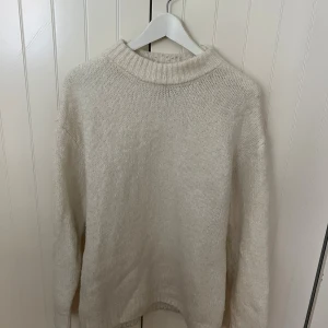 Beige stickad tröja med ribbad krage från Pull & Bear - En stilren beige stickad tröja med ribbad hög krage och muddar. Tröjan har en klassisk passform och är perfekt för lager-på-lager under kyliga dagar. Enkel att matcha med jeans eller andra byxor för en clean look.