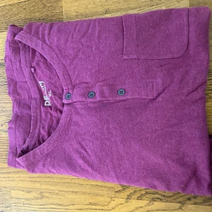 Vinröd långärmad tröja Hampton Republic - Vinröd långärmad tröja från Hampton Republic Denim. Tröjan har rund halsringning, knappslå med tre knappar och en liten bröstficka. Tillverkad i mjuk bomull, perfekt för en avslappnad stil.