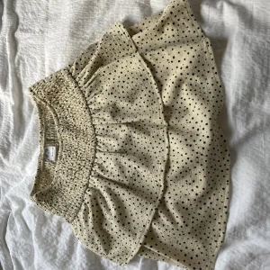Prickig volangkjol från Zara - Snygg beige kjol från Zara med svarta prickar och volangdetalj upptill. Den är gjord i ett lätt, luftigt tyg som passar perfekt till varma dagar. Den har även inbyggda shorts. Perfekta för dig som gillar en söt och trendig stil.