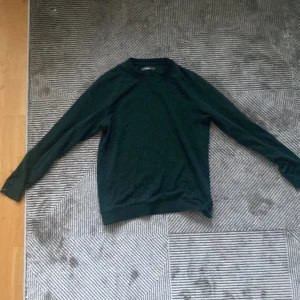 Mörkgrön långärmad tröja Dressmann - En stilren mörkgrön långärmad tröja från Dressmann i klassisk modell. Tröjan har rund halsringning och är tillverkad i mjuk bomull, perfekt för lager-på-lager under höst och vinter. Enkel och clean look som funkar till det mesta.