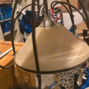 Taklampa med smidesdetaljer och glas - Elegant taklampa med svart smidesram, frostat glas och dekorativa prismor. Fyra armar för ljushållare, klassisk design. Viss smuts och mindre slitage synligt på glaset och metallen, men i gott skick för återbruk. Perfekt för vardagsrum eller matsal.