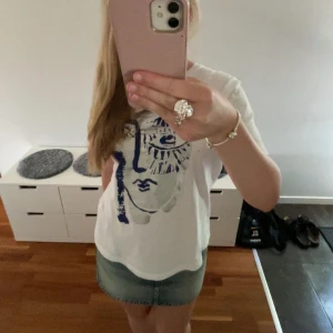 Vit t-shirt med konstnärligt tryck från Zara - Vit t-shirt från Zara med ett stort konstnärligt ansiktstryck i blått och silver på framsidan. Klassisk rund hals och korta ärmar. Skön och mjuk i bomull. (Priset kan diskuteras) 