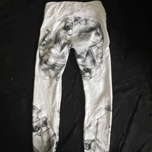 Vita leggings med svart rök-mönster - Säljer ett par vita leggings med unikt svart rök-mönster. De har en tight passform och hög midja, perfekta för att sticka ut. Materialet är mjukt och stretchigt, vilket gör dem bekväma att bära hela dagen.
