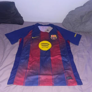 FC Barcelona Lamine Yamal 10 Nike tröja M - Säljer en FC Barcelona matchtröja från Nike med Lamine Yamal och nummer 10 på ryggen. Tröjan är blå och röd med gula detaljer, klubbmärke på bröstet och Dri-FIT-material som andas. Klassisk randig design och korta ärmar. Perfekt för dig som älskar Barca!