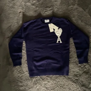 Ami Paris Tröja - Snygg mörkblå stickad tröja från Ami Alexandre Mattiussi med stort vitt hjärta och bokstaven A på bröstet. Tröjan har rund hals, långa ärmar och ribbade muddar. Perfekt för dig som gillar stilrena och trendiga plagg. Passar någon runt 180. Perfekt för hösten och vintern🍂❄️