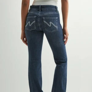 Blå bootcut jeans med broderade fickor - Snygga blå, lågmidjade bootcut jeans med klassisk femficksdesign och broderade detaljer på bakfickorna. 