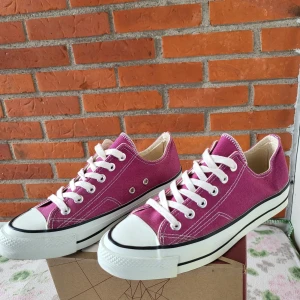 Converse Sneakers, Rosa, Storlek 35 - Ett par rosa Converse sneakers. Perfekt för en avslappnad och trendig stil. Skorna har vita snören och en vit gummisula med en svart rand. "UNI STAR" logotypen finns på baksidan av sulan.