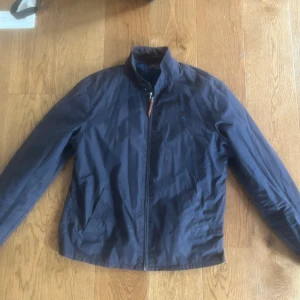 Mörkblå vindjacka från Ralph Lauren - Snygg mörkblå vindjacka från Ralph Lauren med dragkedja framtill och ståkrage. Jackan har två sidofickor och diskret logga på bröstet.