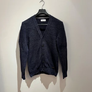 Mörkblå kofta från Pier One - Säljer en stilren mörkblå kofta från Pier One. Koftan har v-ringning, knappar framtill och är långärmad. Materialet är stickat och ger en klassisk look som funkar till många outfits. Perfekt för lager-på-lager under hösten och vintern. Hör av er vid frågor 