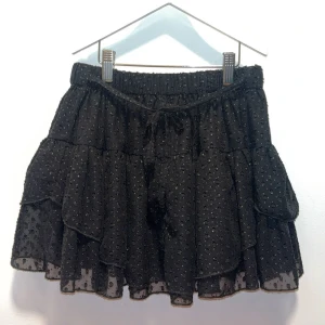 Svart prickig volangkjol från Howtokissafrog - Supersöt svart kortkjol från Howtokissafrog med prickigt mönster och flera lager volanger. Kjolen har elastisk midja med snörning. Står storlek 12y men stor i storleken och passar mig som använder xxs-xs i kjolar! Använt 1 gång.