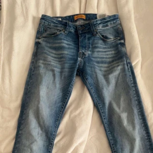 Slim fit Glenn blå jeans - Snygga slim fit Glenn jeans från Jack & Jones i klassisk blå tvätt med slitningar och ljusare partier. Jeansen har fem fickor, normal midja och raka ben. Perfekta för dig som gillar en smalare passform och stilren look.
