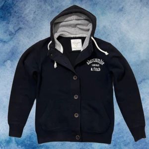 Blå Vintage Kofta Från Abercrombie & Fitch - Snygg Mörkblå vintage kofta från Abercrombie & Fitch med knappar | Observera att etiketten står Storlek L men denna passar som en S, se bild. Modell 175cm, ≈72 kg | Längd 65cm, Bredd amrhåla - amrhåla 52-53 cm