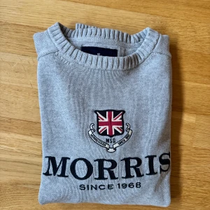 Grå stickad tröja Morris S - Snygg grå stickad tröja från Morris i storlek medium. Tröjan har ett broderat emblem med Union Jack och texten 'Morris Since 1968' på bröstet samt siffran 68 på ena ärmen. Rund hals med ribbad kant och mjukt material som känns skönt mot huden. Storleken är M men den skulle säga att den passar S bättre. Om du har några funderingar är det bara att höra av sig och om du vill få gratis frakt så är det bara att höra av sig innan, så löser vi det🫡🫡