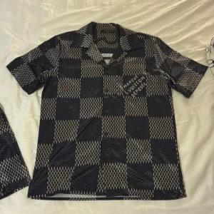 Louis Vuitton rutiga shorts i blått - Säljer ett par sjukt snygga Louis Vuitton shorts med rutigt mönster i mörkblått och beige. De har elastisk midja med snörning och tryckt text på benet. Materialet känns lätt och svalt, perfekt för sommaren. Passformen är normal och designen är riktigt unik.