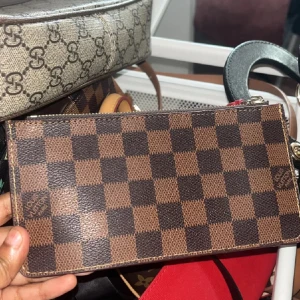 Rutig plånbok  - Snygg plånbok,Slimmad design med dragkedja upptill, perfekt för kort och cash. Ikonisk logga syns på framsidan. Materialet är slitstarkt skinn med lyxig känsla.