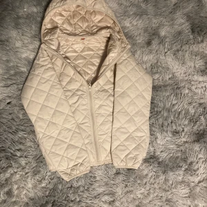 Beige quiltad jacka med huva - Hej! Detta är en väldigt fin jacka som man kan använda medans man tillexempel rider eller om det är kallt ute.kvaleten är väldigt fin samt passform på jackan.