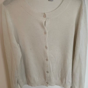 Beige kofta med knappar - En klassisk beige kofta med rund halsringning och knäppning framtill. Tröjan har långa ärmar och ribbade muddar vid ärmslut och nederkant. Perfekt att slänga över en t-shirt eller klänning för en enkel och clean look.