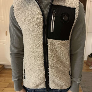 Beige teddyväst limited edition från Snoot - Säljer en beige teddyväst från Snoot med svart bröstficka och dragkedja framtill. Köpt för 1999kr, knappt använd.