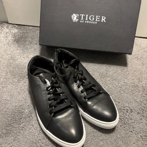  Tiger of Sweden sneaker - Stilrena svarta sneakers från Tiger of Sweden i skinn med vita platta sulor och svarta snören. Klassisk rund tå och minimalistisk design som passar till det mesta. Märkeslogga på insidan och boxen medföljer. Nyskick, ser oanvända ut på insidan.