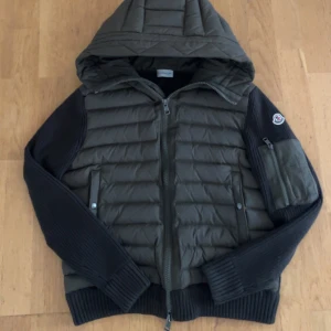Moncler Cardigan Army grön - Snygg Cardigan från Moncler i mörkgrönt med gröna stickade ärmar och detaljer. Jackan har huva, dragkedja framtill och på ärmen samt Moncler-logga på vänster arm. Hör av er vid intresse!