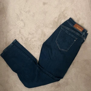 Mörkblå Replay jeans W30 - Snygga mörkblå jeans från Replay i modellen Luzien. Klassisk femficksdesign med gylf och knapp, samt Replay-lapp bak i midjan. Jeansen har raka ben och är tillverkade i slitstarkt denimtyg med snygga detaljer i sömmarna.