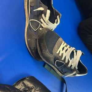 Svarta sneakers med mockadetaljer - Säljer ett par svarta sneakers med vita snören och coola mockadetaljer. Skorna har en rund tå, platt sula och paneler i både textil och mocka. Snygg kontrast mellan svart och vitt, perfekt för dig som gillar en sportig och stilren look.