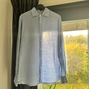 Ljusblå linneskjorta från Kanaljen - Fräsch ljusblå skjorta från Kanaljen i storlek M, tillverkad i 100% linne. Skjortan har klassisk krage, vita knappar framtill och långa ärmar med knapp vid manschetten. Perfekt för dig som gillar en stilren look. Andas bra under tröjor. Säljer då dem är för stor, tycker mer den är Large än Medium.