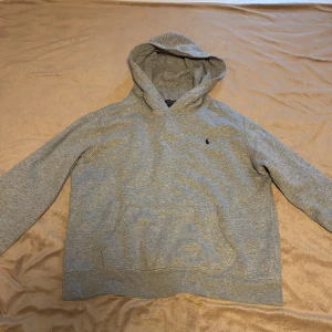 Grå hoodie från Polo Ralph Lauren - Säljer en grå hoodie från Polo Ralph Lauren i storlek S tröjan har huva, känguruficka och det klassiska Polo-logot på bröstet. Mjuk bomullskvalitet och långärmad modell, perfekt för chill dagar. Enkelt och stilrent plagg som funkar till jeans eller joggers.