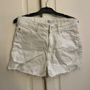 Vita denimshorts med rå kant från Cubus - Snygga vita denimshorts från Cubus i storlek 164. Modellen har klassisk femficksdesign, hög midja och rå, fransig kant nedtill för en cool vibe. Shortsen har knapp och dragkedja framtill samt slitna detaljer vid bensluten. Perfekta för sommarens alla äventyr!