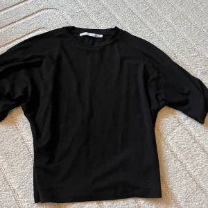 Svart loose topp med kort ärm - En svart topp från 157 med loose passform och korta ärmar. Toppen har rund halsringning och är tillverkad i mjuk bomull, perfekt för en chill och enkel stil. Passar dig som gillar minimalistiskt och bekvämt.