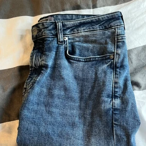 Blå jeans från Dressmann slim fit - Säljer ett par klassiska blå jeans från Dressmann med fem fickor och dragkedja. Jeansen har en rak passform och är tillverkade i slitstarkt denimtyg. Perfekta för dig som gillar en tidlös och enkel stil.