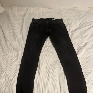 Svarta Replay Grover jeans straight fit - Svarta jeans från Replay, modell Grover med straight fit. Klassisk femficksdesign och normal passform. Jeansen är tillverkade i ett mjukt denimtyg och har diskreta slitningar för en cool look. Perfekta för dig som gillar stilrena svarta jeans.W29 L32 fint skick.