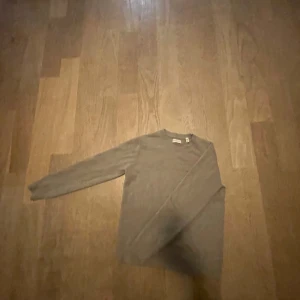 Beige stickad tröja från GANT - Snygg beige stickad tröja från GANT med rund hals och ribbade muddar. Perfekt för dig som gillar klassisk stil med en modern touch. Tröjan har lång ärm och är gjord i mjuk bomull som känns skön mot huden.