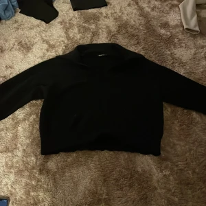 Svart stickad tröja från Gina Tricot - Svart stickad tröja från Gina Tricot med krage och v-ringad öppning. Tröjan har lång ärm och en något croppad passform, perfekt till jeans eller kjol. Enkel och stilren design som funkar året runt. 