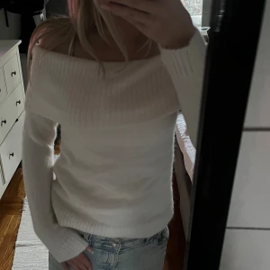 Vit offshoulder stickad tröja - Superfin vit stickad tröja med bred offshoulder-krage. Mjuk och skön, perfekt att styla med jeans eller kjol. Långärmad modell med ribbade muddar och en snygg, avslappnad passform.