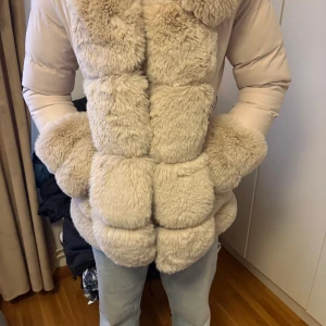 Beige pufferjacka med fuskpäls Copperose - Säljer en beige pufferjacka från Copperose med stora fluffiga pälsdetaljer framtill, på huvan och ärmsluten. Jackan har bälte i midjan och är tillverkad i polyester. Perfekt för dig som vill sticka ut i vinterkylan! Pälsen är äkta och jackan är det inga skador på.