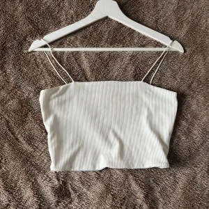 Topp - Säljer en vit linnetopp med smala axelband och ribbad struktur.