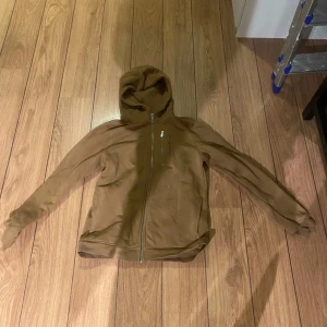 Brun huvtröja från Sail Racing - Snygg brun huvtröja från Sail Racing med dragkedja och en praktisk bröstficka. Perfekt för en avslappnad stil med sin bekväma passform och huva. Storlek 170!