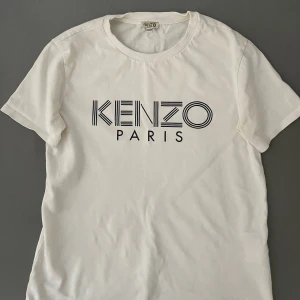 Vit Kenzo t-shirt med logga - Snygg vit t-shirt från Kenzo med stor svart logga på bröstet. Klassisk rund halsringning och korta ärmar. Tillverkad i mjuk bomull för en skön känsla och stilren look.