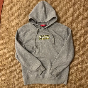 Supreme Leopard print Box logo - Supreme hoodie i grått med huva och snörning. På bröstet finns Supreme-boxlogga med gul leopardmönster. Baksidan har svart text med adress i Shanghai. Mjuk bomullskänsla och ribbade muddar. Perfekt för dig som gillar streetwear och unika detaljer.