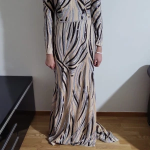 Glittrig långklänning - Snygg långklänning med glittrigt zebramönster i svart, silver och beige✨️Klänningen har långa ärmar, rund halsringning och markerad midja med dekorativ detalj. 