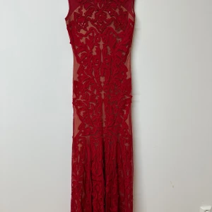 Röd långklänning från Collection 8 - Säljer en maxad röd långklänning från Collection 8 med transparent mesh och broderade detaljer. Klänningen har figurnära passform, är ärmlös och är täckt av röda paljetter och broderier som ger en lyxig känsla. Perfekt för dig som vill sticka ut.