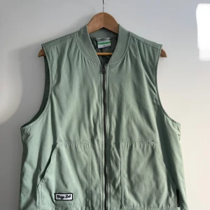 Grön väst med dragkedja från Cropp Lab - Snygg ljusgrön väst från Cropp Lab med två stora fickor framtill och en tydlig dragkedja. Västen har en enkel, rak passform och är tillverkad i mjuk bomull. Perfekt att slänga över en hoodie för en chill look.